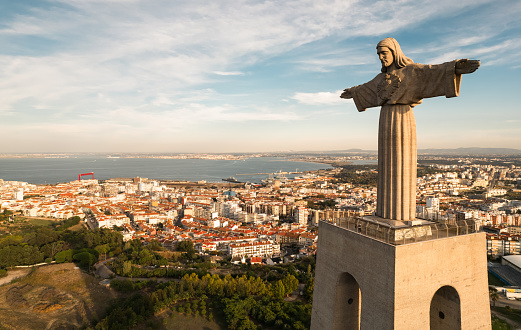 LISBON, PORTUGAL - CIRCA AUGUST, 2021: Sanctuary of Christ the King Catholic monument located against cloudy blue sky in Almada and overlooking Lisbon on sunny day
