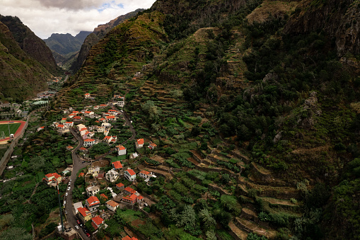 Drone view of houses located on slope of green mountain in village on cloudy day in highlands of Ribeira Brava, Madeira