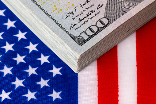 A stack of 100 American dollars bills on the background of a fragment of the American flag