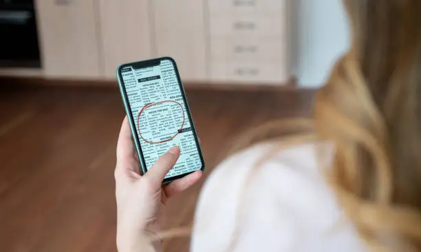 Unrecognizable woman looking at a real estate classified online on her cell phone - For Rent Sign concepts