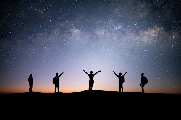 Silhouette small group of young traveler and backpacker watched the star and milky way on top of the mountain with twilight sky. He enjoyed traveling and was successful when he reached the summit. stock photo