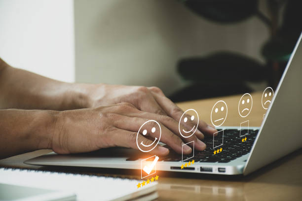Businessman pressing pressing face emoticon on the laptop on desk and selecting smiley face icon and a 5 star rating. Demonstrates that customer satisfaction is essential to a successful business. hombre de negocios presionando el emoticono de la cara presionando en la computadora portátil en el escritorio y seleccionando el ícono de la cara sonriente y una calificación de 5 estrellas. demuestra que la satisfacción del cliente es esencial para u