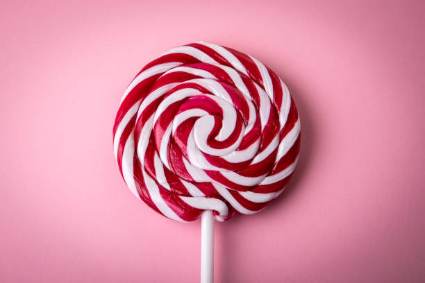pirulito vermelho e branco em um fundo rosa - flavored ice lollipop candy affectionate - fotografias e filmes do acervo