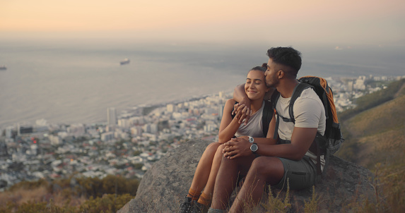 A couple hiking up a mountain on a travel adventure. A happy young man and woman in love looking at the view while exploring nature at sunset