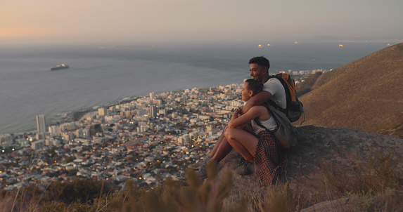 A couple hiking up a mountain on a travel adventure. A happy young man and woman in love looking at the view while exploring nature at sunset