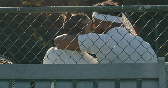 A couple relaxing, playing tennis. A young man and woman in love sharing a romantic moment after playing a game on the court