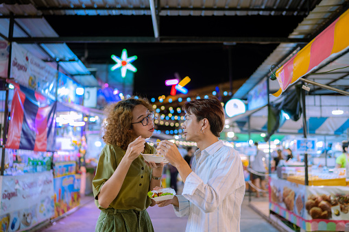 Cheerful couple talking and laughing while walking in the city centre. having fun on the night market and take some snacks.