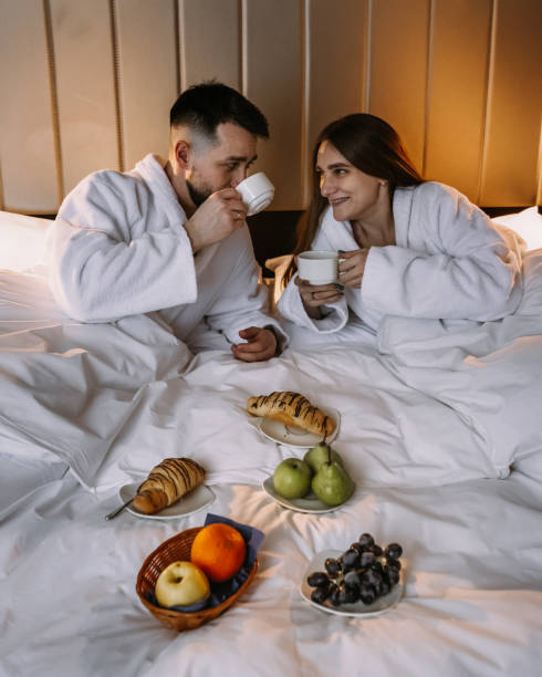 Happy young couple sitting in bed in morning and having breakfast stock photo