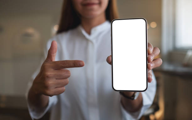 Mockup image of a young woman holding, showing and pointing finger at a mobile phone with blank white screen stock photo