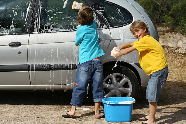 Happy teens playing outside at a car wash. There are girls and guys in their late teens to early twenties. It is summer time and it is warm outside, the teens are wearing shorts, t-shirts, and other summer clothes like baseball hats.