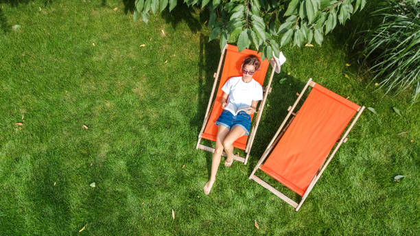 la niña se relaja en el jardín de verano en la tumbona de la tumbona sobre el césped, la mujer lee el libro al aire libre en el parque verde el fin de semana, la vista aérea del dron desde arriba - summer people furniture vacations fotografías e imágenes de stock