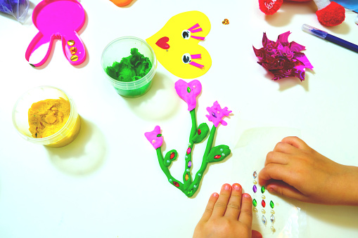 Child making funny crafts  from paper and clay, plasticine. Flowers and hearts  as gift for Mothers day, Birthday or Valentines day . Arts  crafts concept.