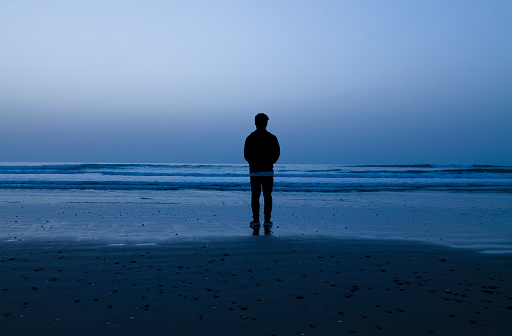 Silhouette of teenage boy standing on beach during sunrise. Cabo de Gata Nature Park, Almeria, Spain