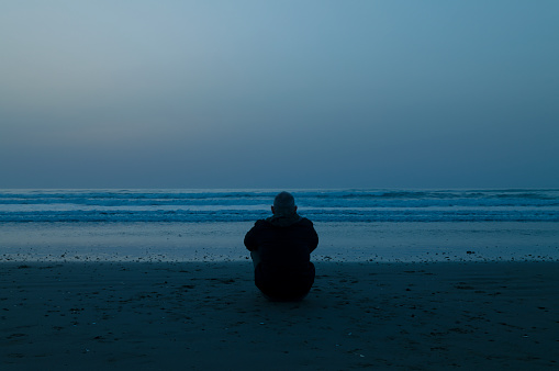 Silhouette of Adult man sitting on beach during sunrise. Cabo de Gata Nature Park, Almeria, Spain