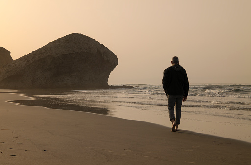 Silhouette of adult man walking on beach during sunrise. Cabo de Gata Nature Park, Almeria, Spain