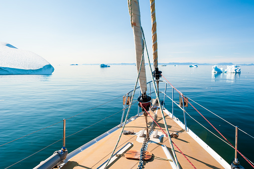 Yacht sailing in Ilulissat icefjord, west coast of Greenland. Atlantic ocean with icebergs, summer seascape