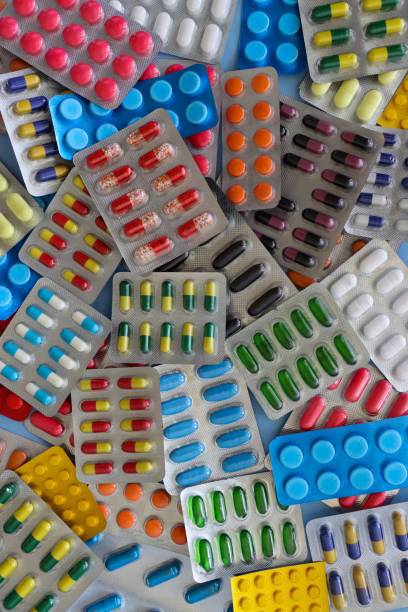 full frame image of heap of pharmaceutical tablet blister packets, pill and gelatine capsule medicines, vibrantly coloured drugs visible through transparent plastic pockets, opaque windows, blue background, elevated view - blister pack pill medicine healthcare and medicine imagens e fotografias de stock