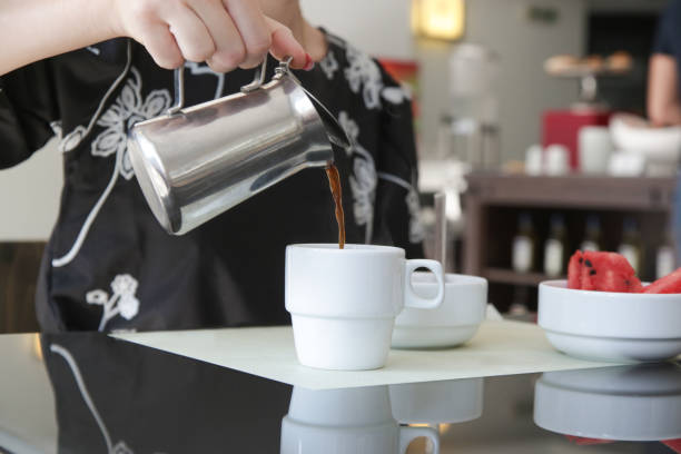 istock Woman's hand holding a coffee mug and pouring it into the coffee cup. Morning routine lifestyle concept, close up 1399138910