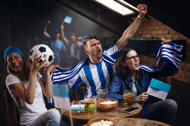 istock Cheerful fans cheering while watching a soccer match on TV in a bar. 1399140633