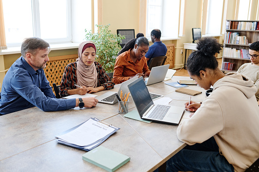 Group of multi-ethnic people having integration and language classes using laptops to do writing task