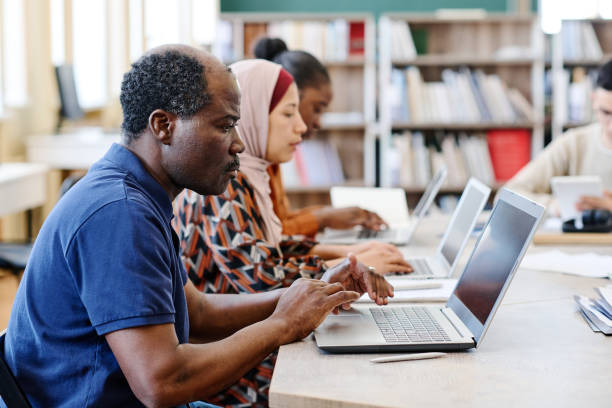 Migrant Students Using Laptops Group of ethnically diverse immigrant students wokring on laptops during lesson searching for information in Internet immigrant stock pictures, royalty-free photos & images