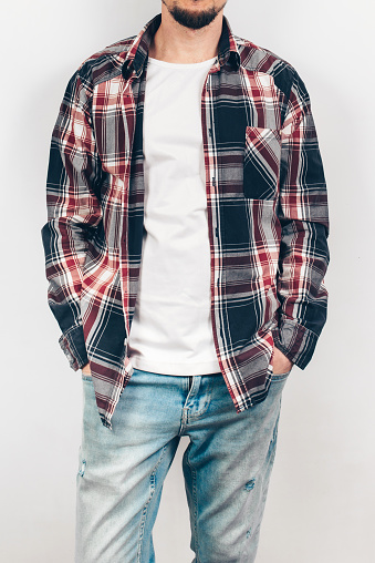 Young man in a plaid shirt against a white wall