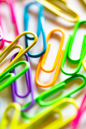 Macro close up of an abundance of vibrant-colored paper clips on a white background.