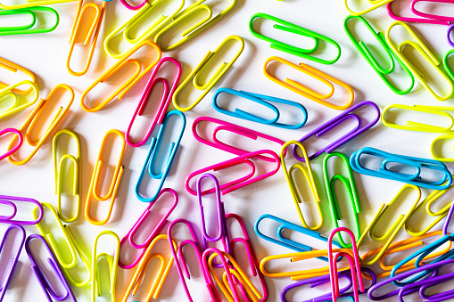Macro close up of an abundance of vibrant-colored paper clips on a white background.