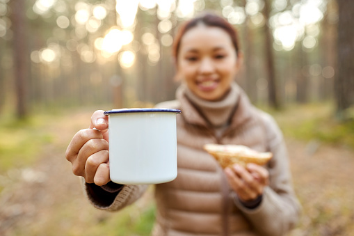 picking season, leisure and people concept - close up of young asian woman with mug drinking tea in autumn forest