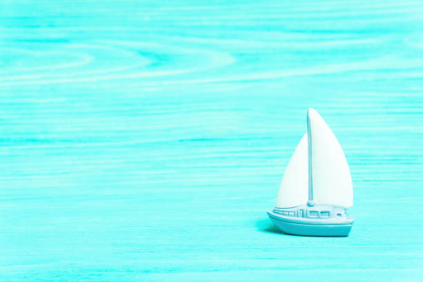 Miniature toy yacht on a turquoise wooden table background imitating water.