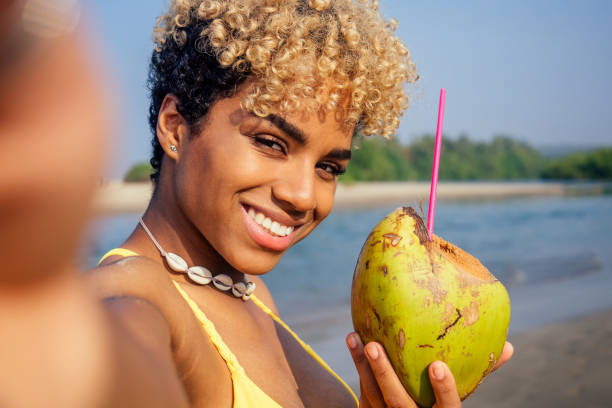 istock hispanic latin beautiful female drinking coco nut water seashells on the neck and taking selfie on camera phone 1399150827