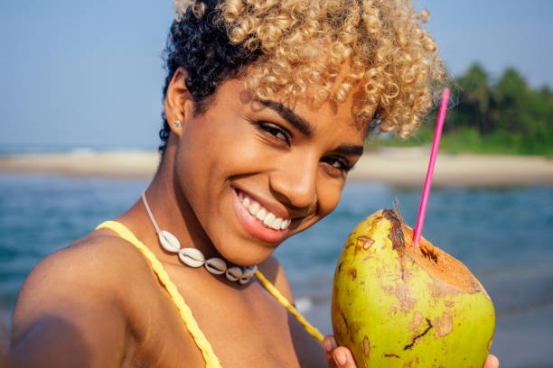 istock hispanic latin beautiful female drinking coco nut water seashells on the neck and taking selfie on camera phone 1399150834