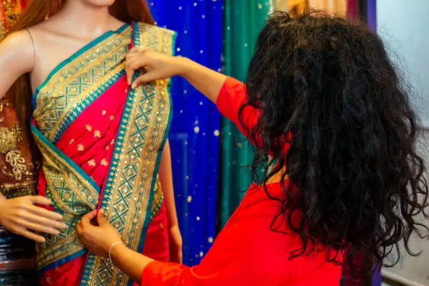 Photo of brunette indian woman choosing a new tradition saree in market.needlewoman designer drapery fabric dress on a mannequin