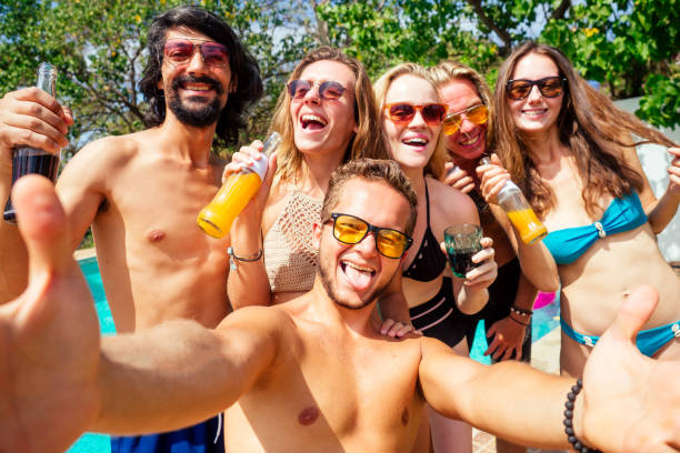 スイミングプールでスマートフォンで自画像を作る魅力的な6人の友人 - party beach indian ethnicity adult ストックフォトと画像
