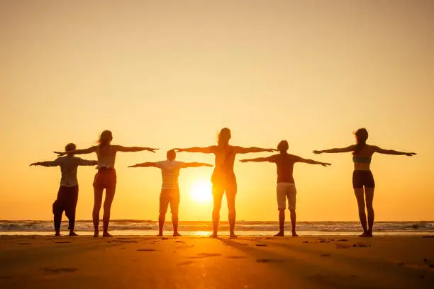 six health people in stand hatha position with hand up raced and breath full chest in Goa India beach at sunset .