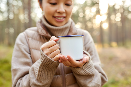 picking season, leisure and people concept - close up of young asian woman with mug drinking tea in autumn forest