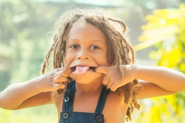 Photo of Mowgli indian boy with dreadlocks hair showing tongue grimacing in tropics green forest background