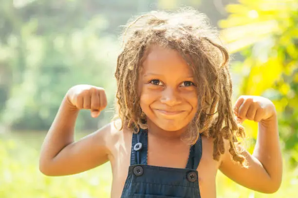 Mowgli indian boy with dreadlocks hair showing muscle arms in tropics green forest background.
