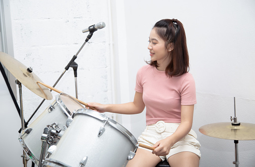 Portrait of young beautiful asian woman playing drums in music studio. She loves and enjoy playing on instruments.Concept of art, support, music, hobby, education.