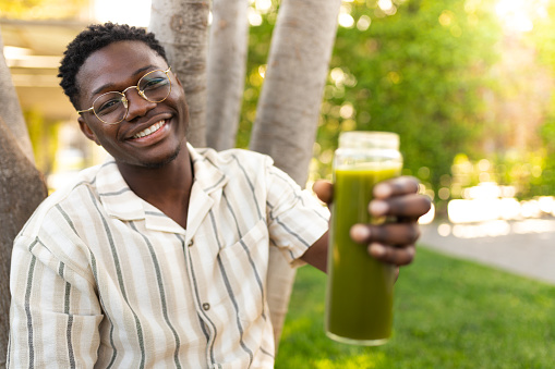 Young black man showing glass bottle of green juice to camera. Focus on man
