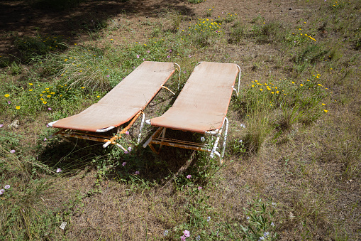 Two red ugly abandoned deck chairs in a decadent garden completely dilapidated.