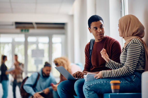 istock Black student using laptop while talking to female friend at university hallway. 1399155925