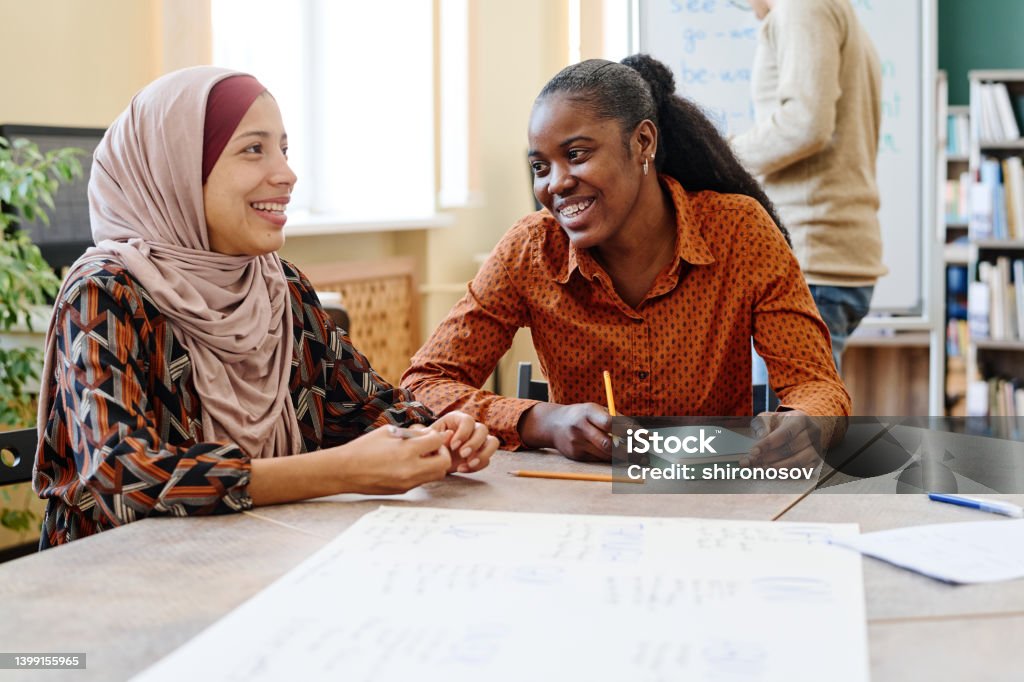 Joyful Women During Lesson Young Black and Middle Eastern women having fun chatting about something during English lesson for immigrants Refugee Stock Photo
