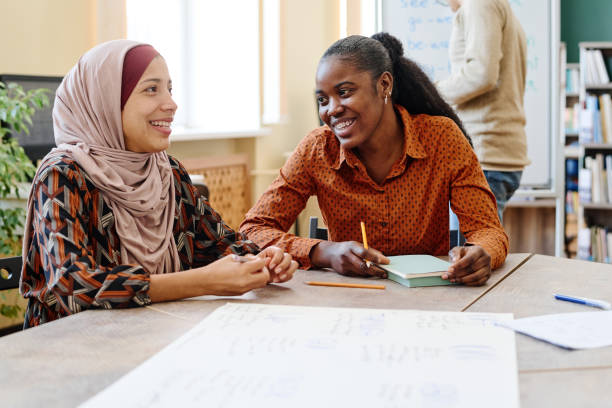 Joyful Women During Lesson Young Black and Middle Eastern women having fun chatting about something during English lesson for immigrants immigrant stock pictures, royalty-free photos & images