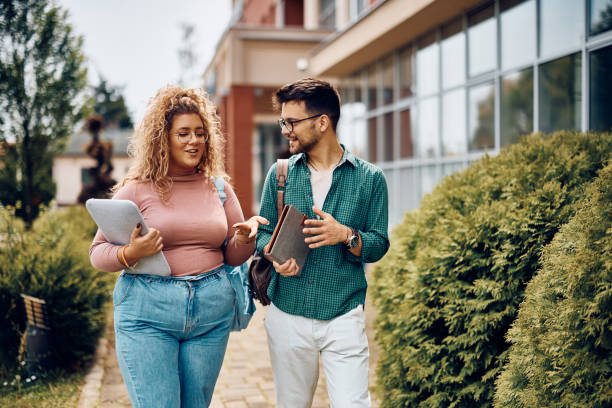 happy student and her male friend communicating while walking through university campus. - campus life imagens e fotografias de stock