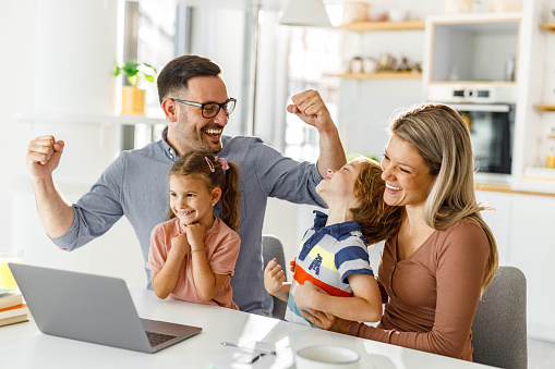Happy parents and their kids celebrating success while using a computer at home.