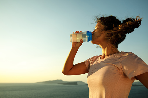 Sweaty female athlete drinking water on a break in summer day. Copy space.