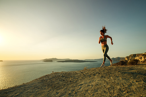 Young female athlete jogging on a hill during summer day above the sea. Copy space.