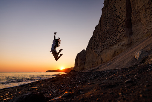 Young carefree woman having fun while jumping on the beach during summer vacation at sunset. Copy space.