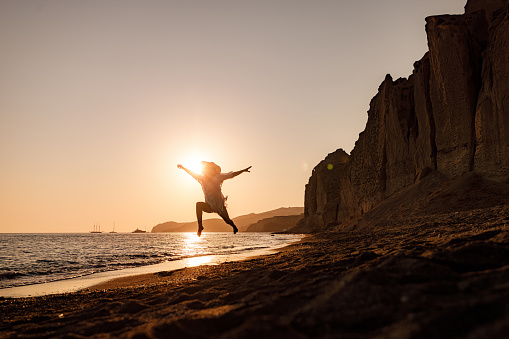 Playful woman having fun while jumping on the beach during summer vacation at sunset. Copy space.